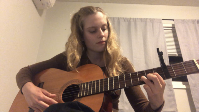 Teagan sits on a bed playing a guitar