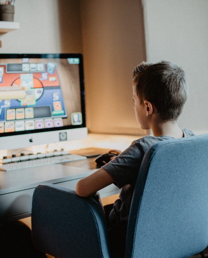 a young boy sits, looking at a MAC computer. He is playing a game.